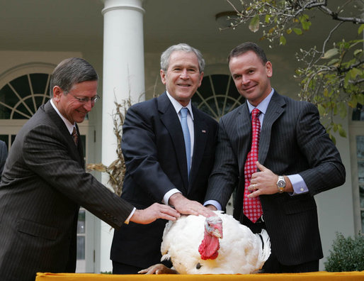 Three men in suits stand around a white turkey in front of the White House